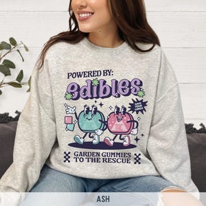 May include: Gray sweatshirt with a graphic of two cartoon gummies with the text "Powered by: edibles" and "Garden gummies to the rescue".