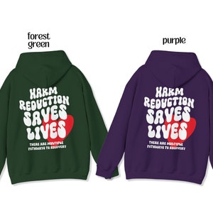 Peut inclure: Deux sweats &agrave; capuche, un vert for&ecirc;t et un violet, avec le texte "HARM REDUCTION SAVES LIVES" en blanc et un c&oelig;ur rouge. Le texte "THERE ARE MULTIPLE PATHWAYS TO RECOVERY" est en dessous. Ils ont tous les deux des capuches et des manches longues.