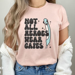 May include: Pink t-shirt with a graphic of a blue thermometer with a face and the text "Not All Heroes Wear Capes".