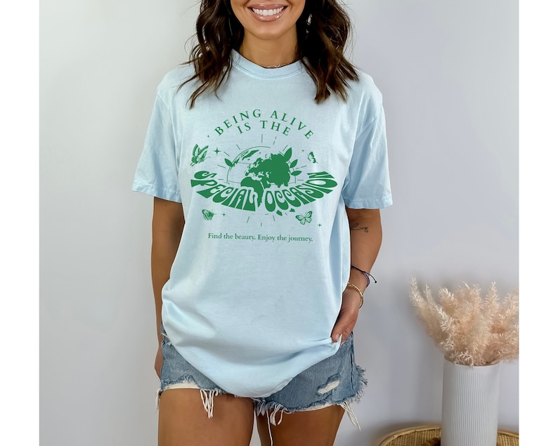 May include: Light blue t-shirt with a green graphic of a globe with butterflies and the text "Being alive is the special occasion. Find the beauty. Enjoy the journey."