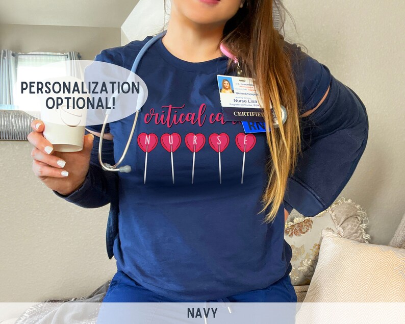Pu&ograve; includere: Maglietta blu navy con il testo "critical care nurse" e grafiche di lecca-lecca rosa. Il testo "CERTIFIED RN" &egrave; su un cartellino identificativo.