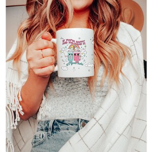 May include: White ceramic mug with a pink, blue and yellow cartoon design of two jars with faces and the text "If you're happy and you know it, sip your magic".
