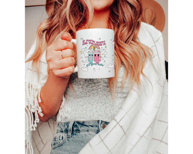 May include: White ceramic mug with a pink, blue and yellow cartoon design of two jars with faces and the text "If you're happy and you know it, sip your magic".