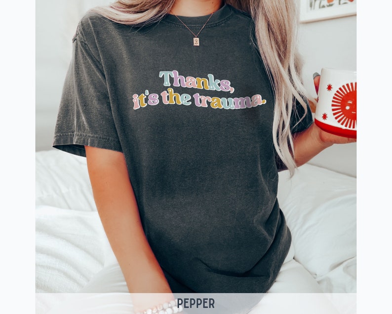 May include: A dark gray t-shirt with the text "Thanks, it's the trauma." in colorful letters.
