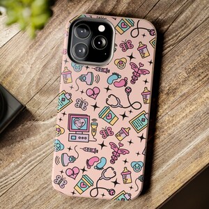 May include: A pink phone case with a pattern of baby-related icons, including a stethoscope, a baby bottle, a pacifier, a footprint, and a heart. The case has a cutout for the phone's camera.