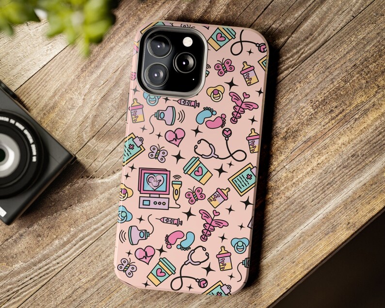 May include: A pink phone case with a pattern of baby-related icons, including a stethoscope, a baby bottle, a pacifier, a footprint, and a heart. The case has a cutout for the phone's camera.