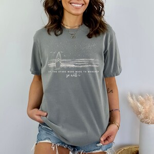 Puede incluir: Camiseta gris con un gr&aacute;fico blanco de una tabla de surf y olas con el texto "Si las estrellas fueron hechas para adorar, yo tambi&eacute;n lo har&eacute;".