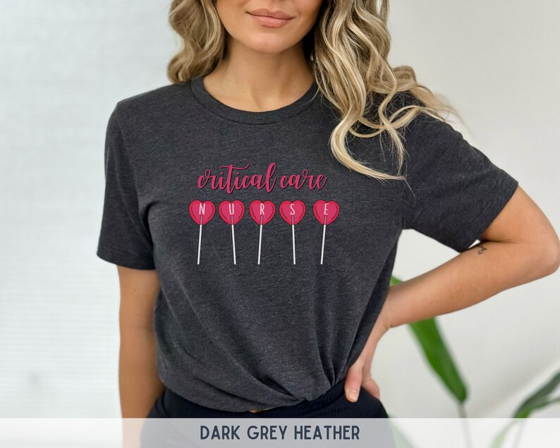 Pu&ograve; includere: Maglietta in jersey grigio scuro con il testo "critical care" e la parola "NURSE" scritta con lecca-lecca a forma di cuore rosa.