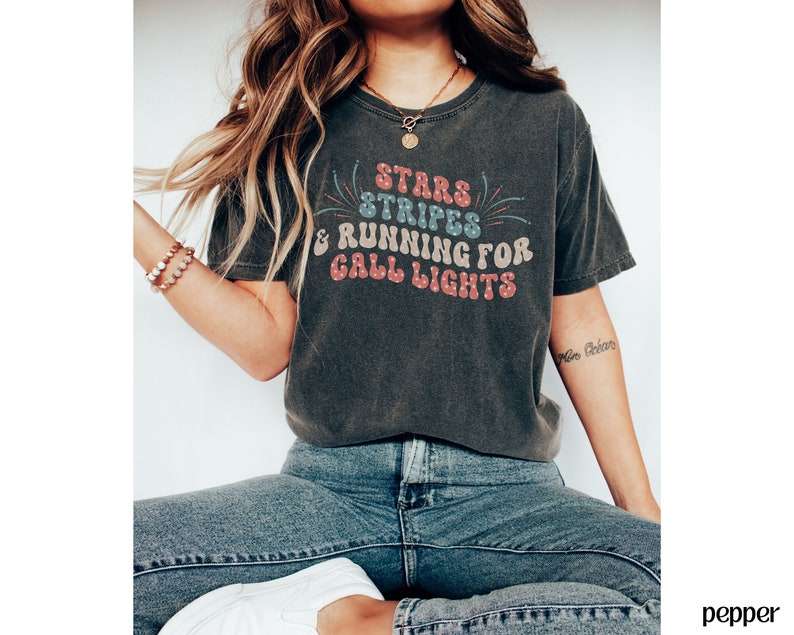 May include: A dark gray t-shirt with a vintage-style graphic that reads "Stars & Stripes & Running for Grill Lights". The graphic is in red, blue, and white with a firework design.