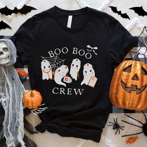 May include: Black t-shirt with a white graphic of three ghosts wearing nurse hats and holding medical supplies. The text "BOO BOO CREW" is printed below the ghosts.