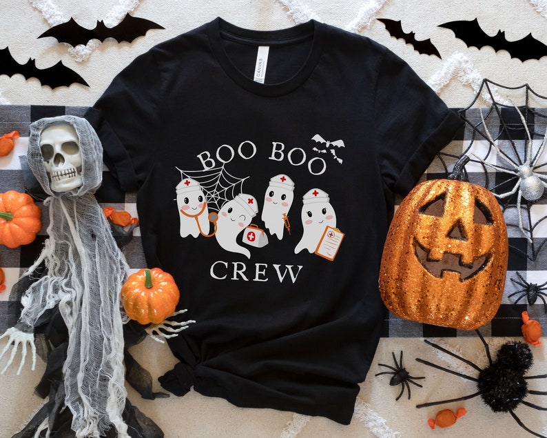 May include: Black t-shirt with a white graphic of three ghosts wearing nurse hats and holding medical supplies. The text "BOO BOO CREW" is printed below the ghosts.