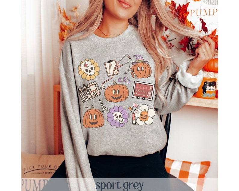 May include: A gray sweatshirt with a graphic print of pumpkins, hearts, and medical symbols. The text "sport grey" is printed on the bottom of the image.
