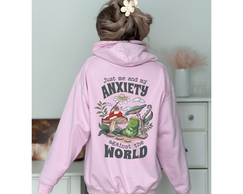 May include: Pink hoodie with a graphic print of a frog, mushroom, and snail with the text "Just me and my anxiety against the world".