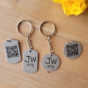 Könnte beinhalten: Silberne Schlüsselanhänger mit QR-Codes und dem Text "JW .org". Die Schlüsselanhänger haben verschiedene Formen: ein Erkennungsmarke, ein abgerundetes Rechteck und ein Kreis. Die Schlüsselanhänger sind an silbernen Schlüsselringen befestigt.
