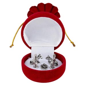 May include: A silver nativity scene set inside a red velvet jewelry box. The box is round with a white satin interior. The nativity figures include Mary, Joseph, a baby, and animals. A gold drawstring is attached.