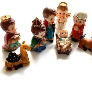 May include: A nativity scene set with figurines of the three wise men, a camel, a donkey, a cow, a sheep, an angel, Mary, Joseph, and baby Jesus in a manger. The figurines are made of painted resin and are approximately 2 inches tall.