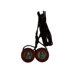 May include: A religious scapular necklace featuring two wooden medallions with religious imagery. The medallions are connected by a dark brown cord. Each medallion has a silver-colored image of a religious figure.