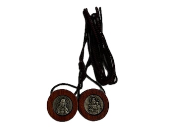 May include: A religious scapular necklace featuring two wooden medallions with religious imagery. The medallions are connected by a dark brown cord. Each medallion has a silver-colored image of a religious figure.