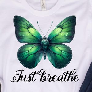 Può includere: T-shirt bianco con un disegno di farfalla verde e la scritta "Just breathe". L'immagine include jeans blu e scarpe da ginnastica grigie.