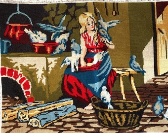May include: A needlepoint tapestry depicting a woman in a red and blue dress surrounded by white doves in a rustic setting. The scene includes a fireplace, a basket, and a wooden stool.