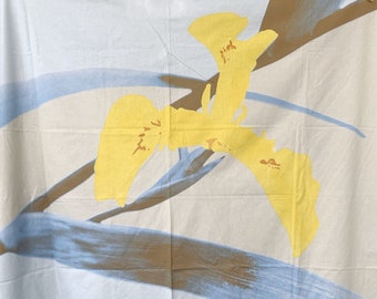 May include: White fabric with a blue and brown abstract design and two yellow iris flowers.