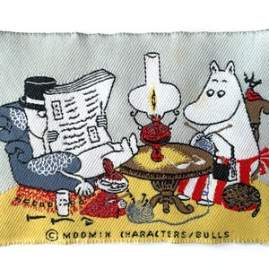 Könnte beinhalten: Ein gewebtes Stoffabzeichen mit einer Cartoon-Szene. Eine Figur liest eine Zeitung, eine andere strickt, und eine dritte sitzt in der Nähe. Eine Lampe und ein Tisch befinden sich in der Mitte. Das Abzeichen hat einen hellgrauen Hintergrund mit gelben und roten Akzenten.