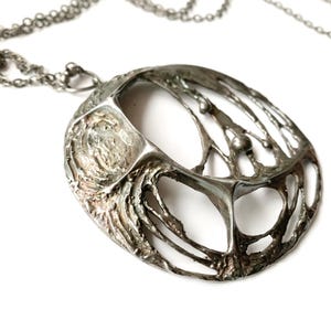 May include: A silver-toned pendant necklace with an abstract, organic design. The pendant features an open, web-like structure with a textured surface and small, spherical accents. The chain is a delicate, linked design.