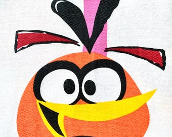 Könnte beinhalten: Nahaufnahme eines Stoffes mit einem Cartoon-Vogel-Design. Der Vogel hat einen orangefarbenen Körper, große weiße Augen, einen gelben Schnabel und schwarze Akzente. Der Hintergrund ist weiß mit grünen und rosa Streifen.
