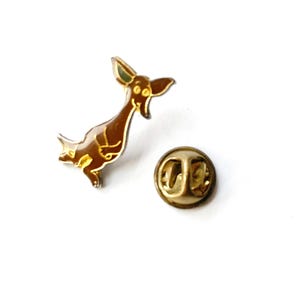 May include: A brown and gold enamel pin featuring a cartoon kangaroo with large ears and a smiling face. The pin has a gold-colored backing and a pin clasp. The kangaroo pin is a fun accessory.