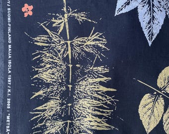 May include: Dark navy fabric with a botanical print featuring gold and silver leaves and a central plant-like design. The text "MARIMEKKO OYJ SUOMI-FINLAND MAIJA ISOLA 1987 / K.I. 2005: 'METSÄ' 100% CO" is printed vertically on the left side.