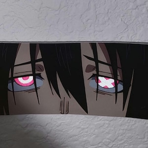 Puede incluir: Una pegatina rectangular con una ilustración de estilo anime de los ojos de un personaje. Los ojos están detallados con detalles rosas y blancos, y el personaje tiene el pelo negro. La pegatina está sujeta por una mano.