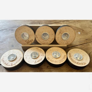 Könnte beinhalten: Acht Holz-Kerzenhalter mit einer kleinen Metallschale in der Mitte jedes. Die Halter sind mit verschiedenen Sprüchen verziert, darunter "Taufe", "Happy", "Du bist ein Geschenk" und "Lieblingsmensch".