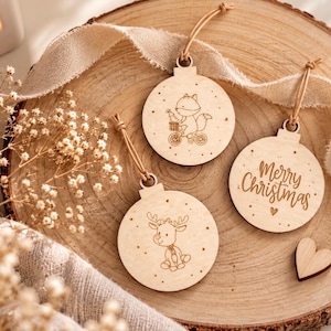 Può includere: Tre ornamenti rotondi in legno chiaro con cordini color cuoio. Uno raffigura una volpe in bicicletta, uno riporta la scritta Merry Christmas con un piccolo cuore, e uno mostra una renna. Ogni ornamento è decorato con piccoli punti incisi.