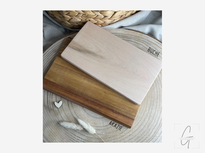 Pu&ograve; includere: Due taglieri rettangolari in legno impilati l'uno sull'altro. Il tagliere superiore &egrave; beige chiaro con il testo BUCHE stampato accanto. Il tagliere inferiore &egrave; in legno marrone pi&ugrave; scuro con il testo AKAZIE stampato accanto. &Egrave; visibile un piccolo cuore bianco.