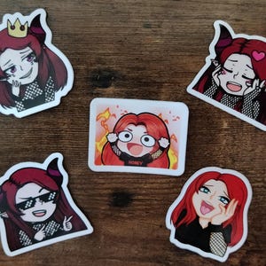 May include: Five colorful stickers featuring cartoon characters with red hair and horns. The characters are wearing black and white outfits and have different expressions. One sticker has the word "Honey" on it.