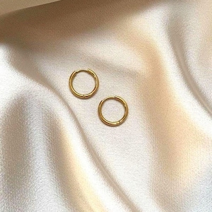 Könnte beinhalten: Zwei goldene Creolen auf einem beigefarbenen Stoffhintergrund.