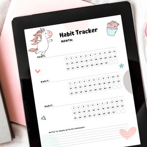 Digital version of the Unicorn Monthly Habit Tracker for submissives on a tablet next to gray and pink books and pink rose petals.
