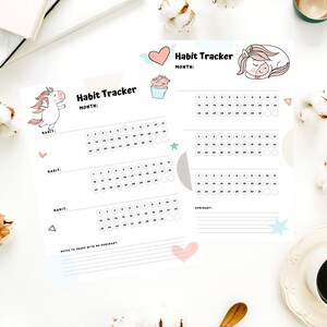 Two samples of the printed habit tracker in the Unicorn Monthly Habit Tracker sheets for submissives on a white desk next to a cup of coffee, flowers, and white notebooks.