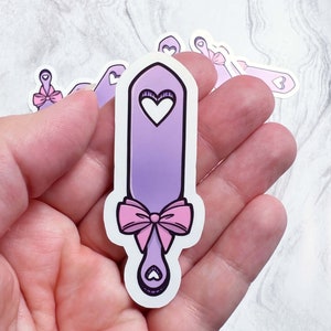 May include: A purple and pink paddle with a heart design and a pink bow. The paddle is a sticker.