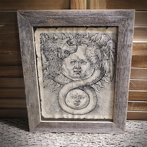 May include: A framed black and white print depicting a detailed illustration of two faces intertwined with a serpent. The top face has a winged creature above it. The artwork is set in a rustic, grey wooden frame.