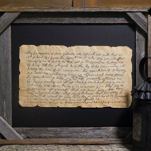 May include: A framed antique document with handwritten text on aged paper. The document is set against a black background within a rustic, gray wooden frame. The text appears to be a historical account or letter.