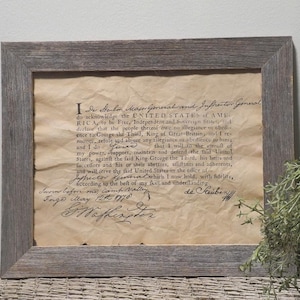 May include: A framed document with a handwritten oath of allegiance to the United States of America. The document is dated May 12th, 1776 and signed by De Kalb. The document is framed in a rustic wood frame.