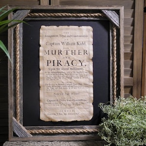 May include: A framed document with a rope border, titled "The Arraignment, Tryal, and Condemnation of Captain William Kidd, for Murther and Piracy, Upon Six Several Indictments." The document is printed in black ink on a white background and includes the date 1701.