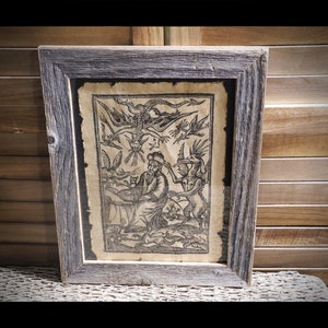 May include: A framed black and white print of a man surrounded by demons and a dragon in the sky. The print is on aged paper and has a rustic wood frame.