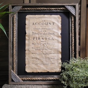 May include: A framed black and white print of an old document titled "An Account of the Conduct and Proceedings of John Gow alias Smith, Captain of the late Pirates, Indicted for Murder and Piracy". The document is framed in a rustic wooden frame with rope accents.