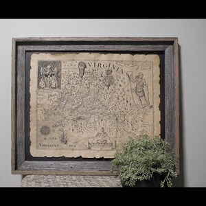 May include: Framed vintage map of Virginia, featuring detailed cartography and historical illustrations. The map is printed on aged paper and set within a rustic, gray wooden frame. The text "VIRGINIA" is prominently displayed. A small plant in a dark pot sits below the frame.