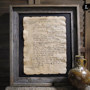 May include: A framed document with handwritten text in black ink on aged paper. The document is displayed on a dark background. The frame is made of rustic wood with a weathered finish. A brown ceramic jug with a bearded face design is in the foreground.