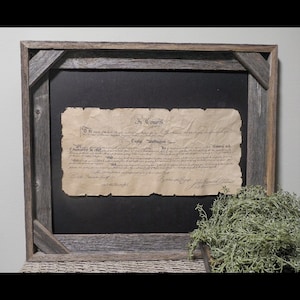 May include: A framed document with the text "In Congress" and the name "George Washington." The document has an aged, parchment-like appearance, set against a black background. The frame is made of rustic, weathered wood.