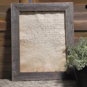 Peut inclure: Un document encadré avec du texte manuscrit. Le cadre est en bois gris vieilli. Le papier à l'intérieur est vieilli et jauni, avec des plis visibles. Le texte est à l'encre noire.