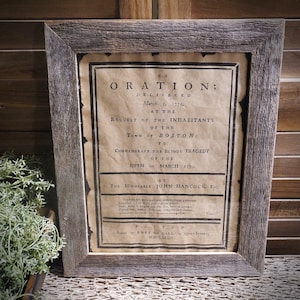 May include: A framed print of a historical document titled "ORATION; DELIVERED March 5. 1774, AT THE REQUEST OF THE INHABITANTS OF THE TOWN OF BOSTON: TO COMMEMORATE THE BLOODY TRAGEDY OF THE FIFTH or MARCH 177... BY THE HONORABLE JOHN HANCOCK, Esq;" The print is on aged paper with a brown background and is framed in a rustic wood frame.
